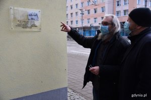 Marek Stępa, naczelnik Wydziału Ochrony Dziedzictwa Urzędu Miasta Gdyni (po prawej) przygląda się montażowi tablicy pamiątkowej, która jest umieszona na żółtej fasadzie budynku na rogu ulic Świętojańskiej i Derdowskiego. Jeden z mężczyzn pracujących przy montażu wskazuje na tablicę // fot. Sławomir Okoń