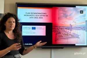 Kobieta prowadząca prezentację w sali konferencyjnej. Stoi obok ekranu wyświetlającego slajdy na temat Planu zrównoważonej mobilności dla Gdyni na lata 2026-2035..