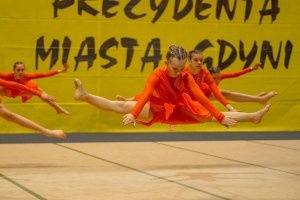 Zawodniczki w kolorowych strojach w pozach gimnastycznych na scenie