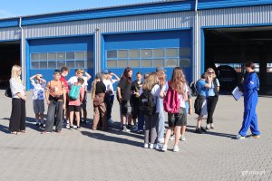 Grupa ludzi przed hangarem 