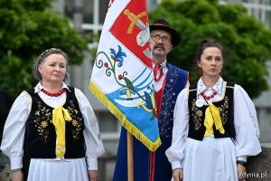 Osoby w ludowych strojach i sztandar kaszubski