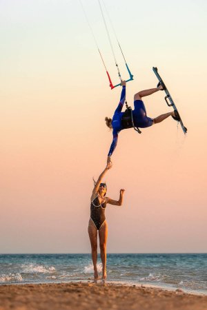 Kobieta na desce do kitesurfingu podająca rękę kobiecie stojącej na brzegu morza