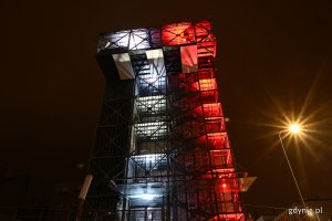 Budynek InfoBoksu oświetlony na biało-czerwono. Obok świecąca latarnia // fot. Michał Puszczewicz