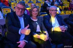 Hala Polsat Plus Arena Gdynia, trybuny, przyciemnione światło, trzy osoby pozują do zdjęcia