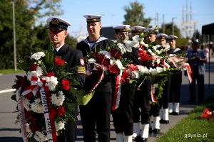 Marynarze stoją w rzędzie. Każdy z nich ma w rękach wieniec lub wiązankę kwiatów // fot. Przemysław Kozłowski