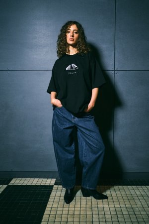 W kolekcji marki Diverse znalazły się między innymi T-shirty. Modelka w kręconych włosach pozuje w koszulce na tle Muzeum Emigracji w Gdyni