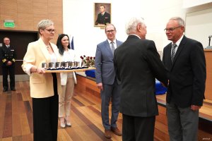 Mężczyźni w garniturach, kobieta w ż&oacute;łtej marynasrce trzyma tacę z odznaczeniami