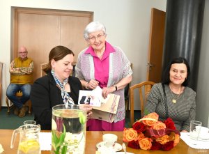 Kobieta w ciemnej marynarce ogląda fotografie, kt&oacute;re pokazuje pani w r&oacute;żowej bluzsce