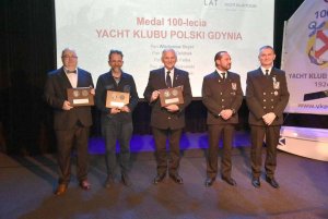 Grupa osób stojących na scenie i mających za plecami biały ekran