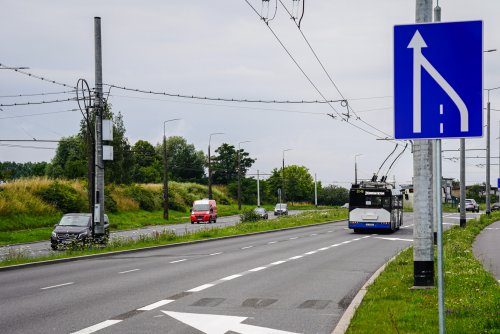 Ulica Wielkopolska, widoczne pasy ruchu w kierunku Dąbrowy, na prawym pasie biało-granatowy trolejbus, na pierwszym planie znak drogowy - zwężenie pasa ruchu