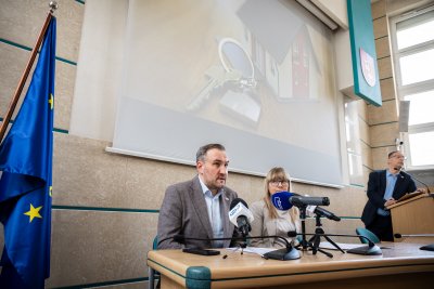 Sala w urzędzie miasta, stół prezydialny, do mikrofonów wypowiadają się Tomasz Augustyniak i Joanna Wasilewska, w tle na ekranie zdjęcie makiety domu i kluczy
