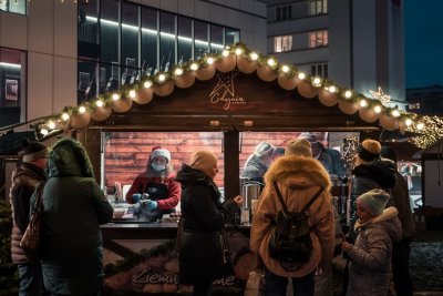 Plac Grunwaldzki po zmierzchu. Drewniana budka z napisem Gdynia, w środku pracownik. Na zewnątrz przechodnie
