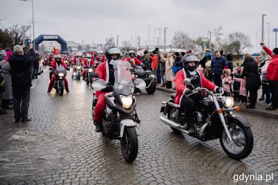 Aleja Jana Pawła II w Gdyni. Zima, deszcz. Kilkadziesiąt motocykli i ludzi w przebraniach Mikołajów. Na chodniku publiczność.
