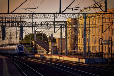 Perony dalekobieżne w Gdyni Głównej. Do peronupodjeżdża niebiesko-pociąg Polregio. Zachodzące słońce w tle