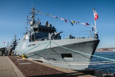 Okręt ORP Mewa przy nabrzeżu Pomorskim. Widoczna biało-czerwona bandera na rufie, obok spacerujący ludzie, gala banderowa na okręcie. Słoneczny dzień