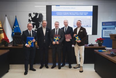 Sala konferencyjna, do zdjęcia z teczkami w rękach pozują Marcin Skwierawski, Mieczysław Struk, Dariusz Nałęcz, Stanisław Cirocki i Leszek Bona, w tle ekran z wyświetlaną nazwą projektu dotyczącego szpitala w Gdyni, flagi Pomorza, Polski i Unii Europejskiej