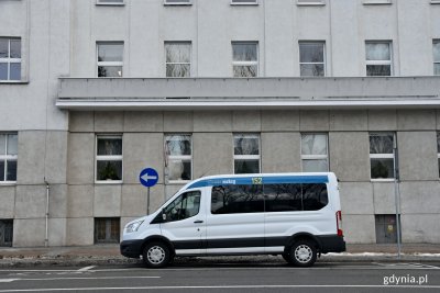 Biały bus przeznaczony do transportu osób z niepełnosprawnościami oraz sprzętu. Samochód zaparkowany jest przed budynkiem Urzędu Miasta Gdyni (al. Marsz. Piłsudskiego 52/54)