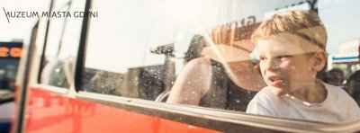Twarz chłopca widoczna w szybie zabytkowego, czerwono-beżowego trolejbusu