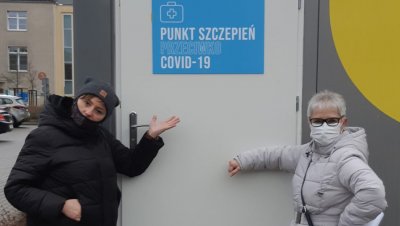 Na zdjęciu dwie kobiety ubrane w zimowe ubrania i maseczki zasłaniające usta i nos. Stoją przed wejściem do punktu szczepień przeciwko COVID-19.