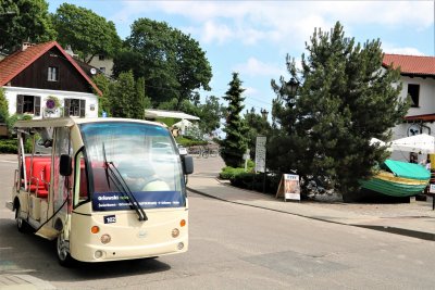 Ulica Orłowska. Na asfalcie zaparkowany beżowy meleks z napisem Orłowski meleks. W tle zieleń, budynki.