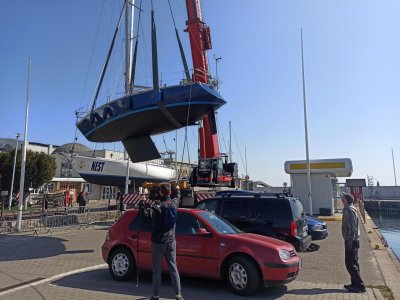Nabrzeże mariny w Gdyni. Widoczny jacht na podnośniku, w powietrzu. Na nabrzeżu ludzie, którzy obserwują wodowanie