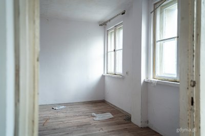 Zdjęcie pustego mieszkania, białe ściany, widoczne dwa okna z podziałką