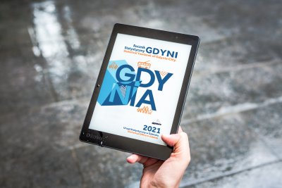 Ręka trzyma tablet, na ekranie okładka Rocznika Statystycznego Gdyni, w tle szara podłoga