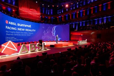 Duża scena z dużym ekranem. Na ekranie napisy imprezy ABSL Summit 2022. Widać zgromadzoną przed sceną widownię oraz prelegenta na scenie.