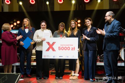 Scena w kościele w Małym Kacku, na scenie pozują do zdjęcia: dwoje prowadzących ze stowarzyszenia KACK, troje członków grupy teatralnej, przedstawiciele sponsorów i współorganizatorów, widoczna plansza z nagrodą w wys. 5000 złotych