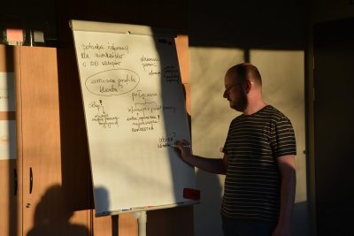 Mężczyzna w okularach pisze markerem po białej tablicy, robi strzałki i wpisuje hasłowo równoważniki zdań