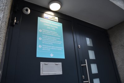 Szare drzwi z wrzutnią i jasnoniebieska tablica informacyjna
