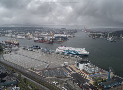 Zdjęcie lotnicze. Widoczne nabrzeże portu w Gdyni, basen portowy, budynki, nowy terminal. Przy terminalu płynie prom z logo Polferries. Deszczowa pogoda.