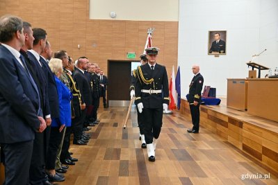 Sala w Akademii Marynarki Wojennej, ludzie w mundurach na widowni, na środku sali wchodzi poczet sztandarowy ze sztandarem