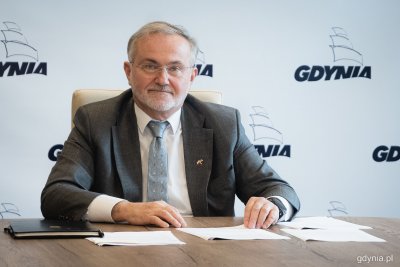 Na zdjęciu uśmiechnięty niebieskooki mężczyzna siedzi przed laptopem