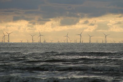 Morze, częsciowo zachmurzone niebo, na linii horyzontu kilkanaście turbin wiatrowych