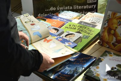 Czytelnik przeglądający jedną z książek dla dzieci dostępnych w gdyńskiej księgarni. W tle: kolorowe okładki. (fot. Paweł Kukla)
