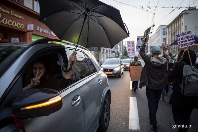 Jedna z ulic w centrum Gdyni, po lewej stronie samochód uczestniczący w proteście, po prawej protestujący tłum z transparentami