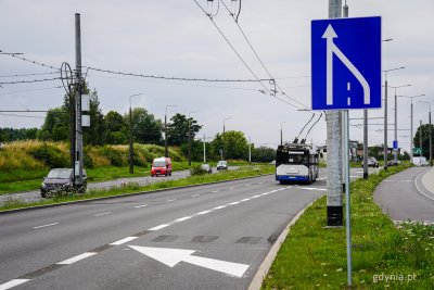 Ulica Wielkopolska, widoczne pasy ruchu w kierunku Dąbrowy, na prawym pasie biało-granatowy trolejbus, na pierwszym planie znak drogowy - zwężenie pasa ruchu