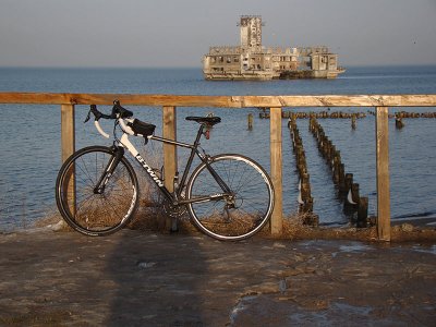 Plaża w Babich Dołach, rower oparty o drewnianą barierkę, plaża, skarpa, morze, w tle torpedownia