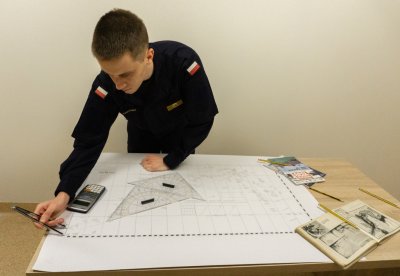 Janusz Adrianek w mundurze pochyla się nad stołem, na którym leży mapa