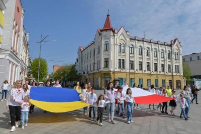 Grupa dzieci na placu w Żytomierzu. Trzymają polską i ukraińską flagę. W tle zabytkowe kamienice