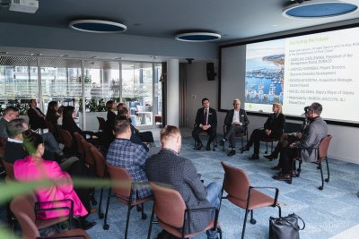 Sala konferencyjna, zdjęcie na ekranie, kilka osób siedzi na krzesłach na środku, ludzie na widowni