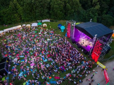 Na zdjęciu uczestnicy koncertyu pod gołym niebem, siedzą na kocach, atmosfera jest niezobowiązująca