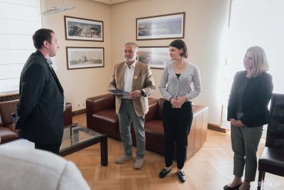 Cztery osoby w gabinecie. Stoją naprzeciwko siebie.