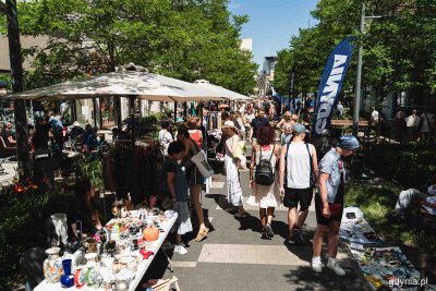 Woonerf na Abrahama, słoneczny dzień, stragany po bokach ulicy, ludzie idą środkiem, oglądają rzeczy, widoczne kamienice i miasto