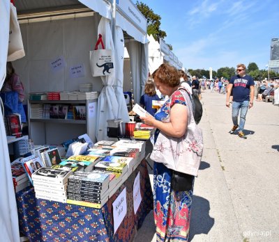 Kobieta w kolorowej sukience przy jednym ze stoisk z książkami na bulwarze Nadmorskim podczas Nadmorskiego Pleneru Czytelniczego (zdjęcie archiwalne)