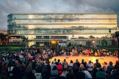 Zdjęcie z ubiegłorocznej, 10. edycji festiwalu „Pociąg do Miasta”. Publiczność zgromadzona w zielonej strefie między budynkami III i IV Pomorskiego Parku Naukowo-Technologicznego przed pokazem sztuki „Q&A (the Polish Edition)” (fot. Krzysztof Winciorek)