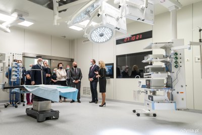Wnętrze nowej sali operacyjnej. Widoczny sprzęt medyczny i stół operacyjny. W tle grupa osób.