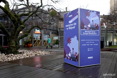 Tzw. kubik stojący na tle gdyńskiego InfoBoxu. Na plakacie napisy: Rok zaczyna się w Gdyni! Wesołych Świąt Bożego Narodzenia! Fot. Przemysław Kozłowski.