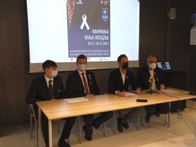 czterech mężczyzn siedzi przy stole na którym stoją mikrofony w tle plakat konferencji